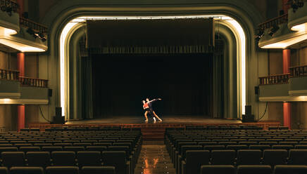 Man and woman dancing together on stage near empty seats during rehearsal in dim theater - ADSF36412