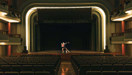 Mann und Frau tanzen zusammen auf der Bühne in der Nähe von leeren Sitzen während einer Probe in einem schummrigen Theater - ADSF36412