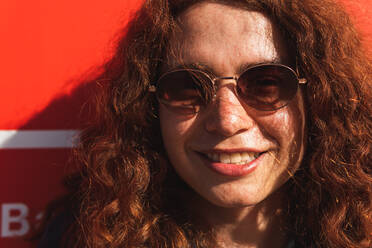Porträt einer lächelnden jungen Frau mit Sonnenbrille, die an der Wand steht - ADSF36425