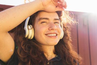 Porträt einer jungen Frau mit Hand im Haar, die Kopfhörer trägt und an der Wand steht - ADSF36434