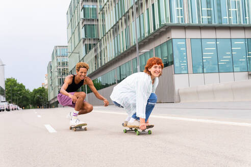 Ganzer Körper von glücklichen multiethnischen Freunden in Freizeitkleidung fahren Skateboards auf Asphalt Fahrbahn, während sie Spaß zusammen in der Stadt - ADSF36469