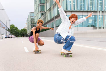 Ganzer Körper von glücklichen multiethnischen Freunden in Freizeitkleidung fahren Skateboards auf Asphalt Fahrbahn, während sie Spaß zusammen in der Stadt - ADSF36470
