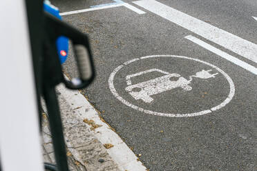 Weißes Schild zum Aufladen eines Elektroautos auf einer asphaltierten Straße auf einem Parkplatz mit einer öffentlichen Station auf einer Straße der Stadt - ADSF36478