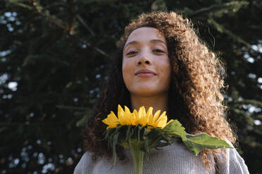 Lächelnde junge Frau mit Sonnenblume an einem sonnigen Tag - AMWF00748