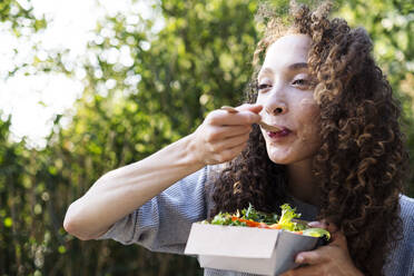 Young woman eating vegetable salad in park on sunny day - AMWF00749