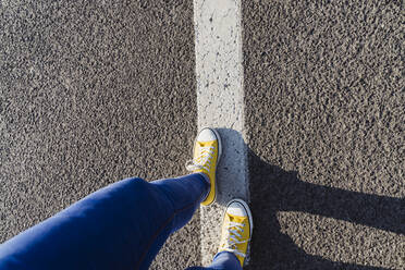 Woman wearing canvas shoes walking on dividing line - OSF00793