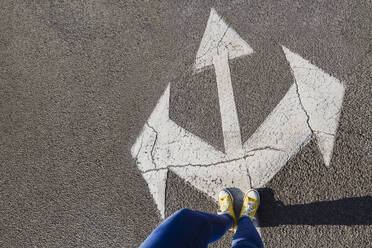 Woman standing on three way direction arrow sign on road - OSF00794