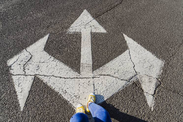 Woman standing on asphalt with three way direction arrow sign - OSF00799