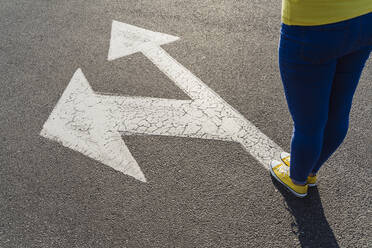 Woman wearing canvas shoes standing on arrow sign - OSF00803