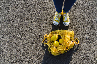 Frau steht neben einem Netzbeutel mit Zitronen auf Asphalt - OSF00810