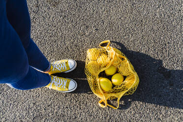 Frau steht auf Asphalt neben einer Netztasche mit Zitronen - OSF00811