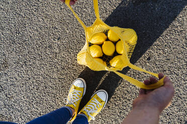 Frau steht auf der Straße und öffnet eine Netztasche mit Zitronen - OSF00812