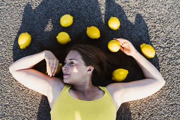 Smiling woman lying down on asphalt with lemons - OSF00824