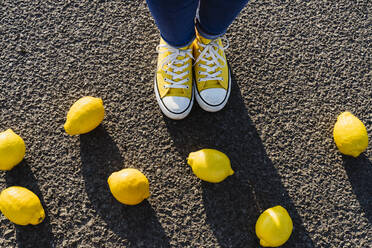 Woman wearing canvas shoes standing near lemons on asphalt - OSF00825