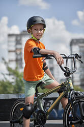 Smiling boy wearing cycling helmet sitting on BMX bike - ZEDF04749
