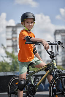Smiling boy wearing cycling helmet sitting on BMX bike - ZEDF04749