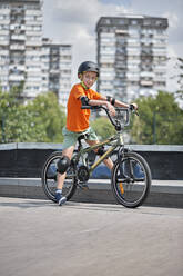 Junge mit Sicherheitsausrüstung auf BMX-Rad in Skateboard-Park sitzend - ZEDF04750