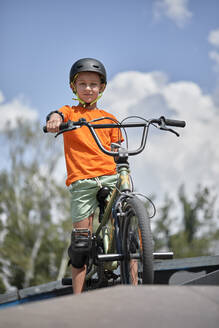 Boy sitting on BMX bike at sports ramp - ZEDF04752