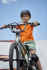 Determined boy sitting on BMX bike at skateboard park - ZEDF04761