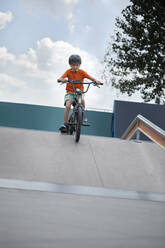 Boy riding BMX bike at skateboard park in front of sky - ZEDF04762