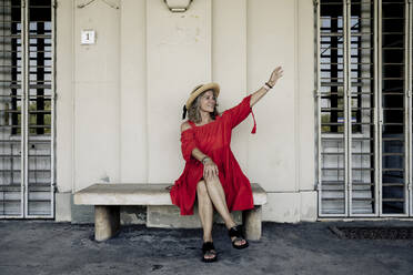 Smiling woman waving sitting on bench at railroad station - FLLF00666