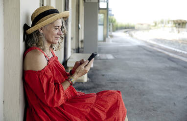 Woman using smart phone sitting at train station - FLLF00669