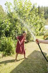 Mädchen spielt mit Wasser durch einen Schlauch im Garten an einem sonnigen Tag - LESF00093