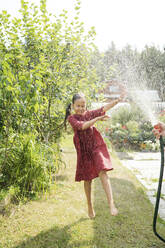 Carefree girl dancing in water from hose at garden - LESF00094