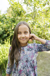 Lächelndes Mädchen hält Apfel in der Nähe des Ohrs im Garten - LESF00100