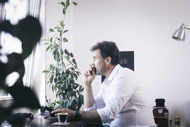 Thoughtful businessman sitting at office coffee corner - MMFF01342