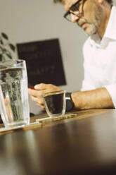 Trinkglas und Espressotasse auf Tisch mit Geschäftsmann im Hintergrund - MMFF01353