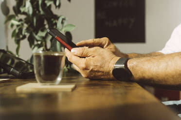 Hände eines Geschäftsmannes, der eine intelligente Uhr trägt und ein Mobiltelefon in einer Kaffee-Ecke im Büro benutzt - MMFF01361