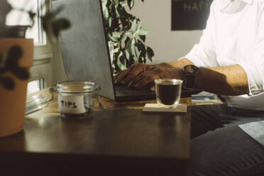 Businessman working on laptop by espresso cup at office coffee corner - MMFF01366