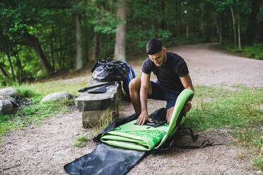 Man folding paddleboard by bench - DMMF00041