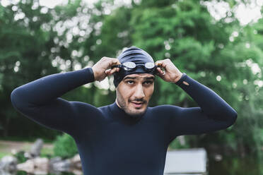 Mann im Neoprenanzug beim Einstellen der Schwimmbrille - DMMF00049