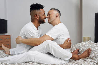 Romantic gay couple nuzzling on bed at home - GGGF01081