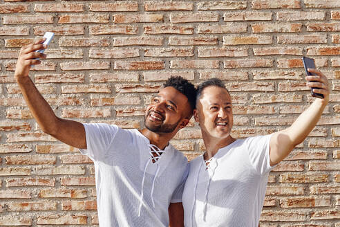 Männer, die Selfies mit ihren Handys vor einer Ziegelmauer machen - GGGF01086