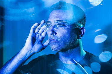Man adjusting futuristic glasses illuminated with blue light - JSMF02404