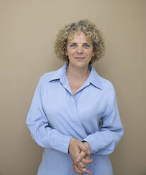 Businesswoman with hands clasped against brown background - HMEF01388