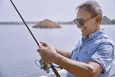 Happy senior man with fishing rod standing by sea - AZF00455