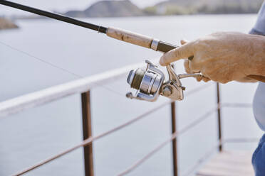 Hand's of senior man with fishing tackle at jetty - AZF00456