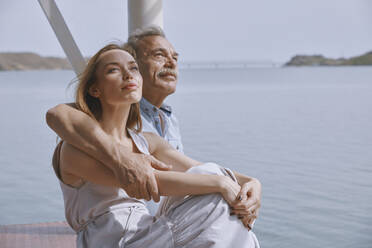 Nachdenklicher älterer Mann sitzt mit seiner Tochter am Steg am Meer - AZF00460