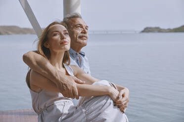 Thoughtful senior man sitting with daughter at jetty by sea - AZF00460