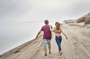 Vater und Tochter spazieren zusammen auf Sand bei Sonnenuntergang - AZF00464