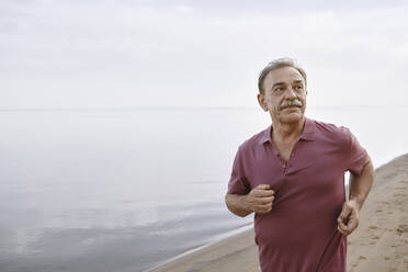 Thoughtful senior man running by sea at beach - AZF00467