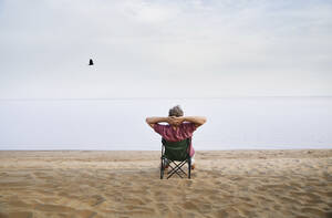 Älterer Mann sitzt auf einem Klappstuhl und entspannt sich am Strand - AZF00468
