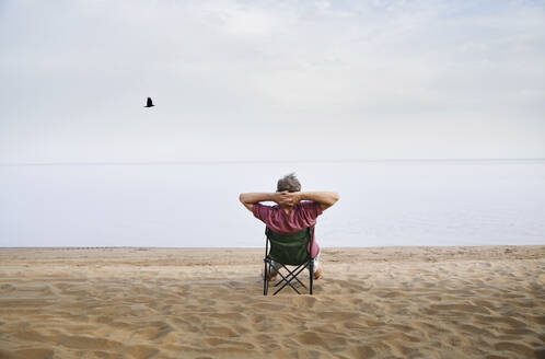 Senior man sitting on folding chair relaxing at beach - AZF00468