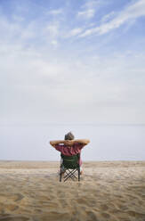 Mann sitzt entspannt auf einem Klappstuhl am Strand - AZF00469
