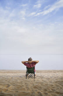 Man relaxing sitting on folding chair at beach - AZF00469