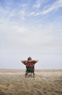 Mann sitzt entspannt auf einem Klappstuhl am Strand - AZF00469